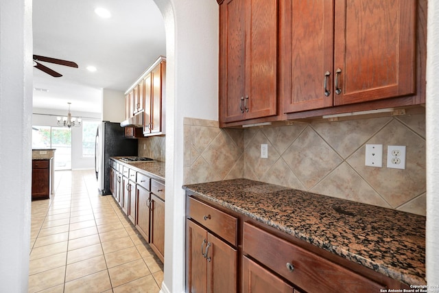 kitchen with light tile patterned flooring, ceiling fan with notable chandelier, tasteful backsplash, dark stone counters, and hanging light fixtures