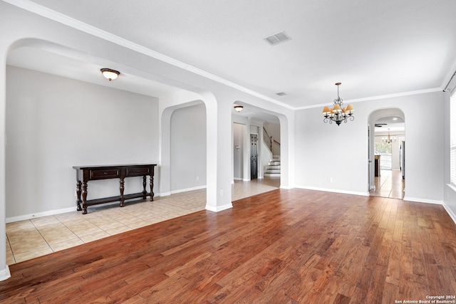 unfurnished living room featuring an inviting chandelier, crown molding, and light hardwood / wood-style floors