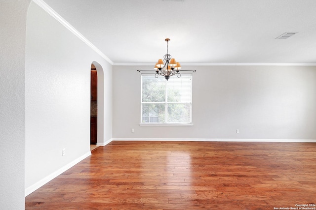 empty room featuring wood-type flooring, a notable chandelier, and crown molding