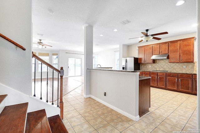 kitchen with light tile patterned floors, dark stone countertops, backsplash, gas stovetop, and stainless steel fridge with ice dispenser