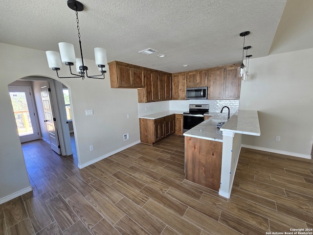 kitchen featuring appliances with stainless steel finishes, sink, kitchen peninsula, decorative light fixtures, and dark wood-type flooring