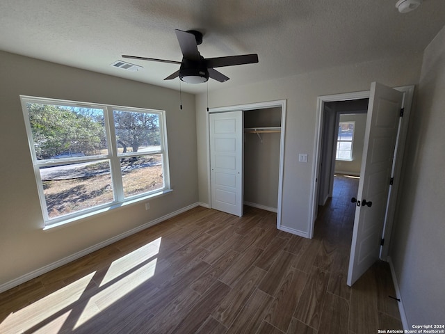 unfurnished bedroom featuring dark wood-type flooring, ceiling fan, a closet, and multiple windows