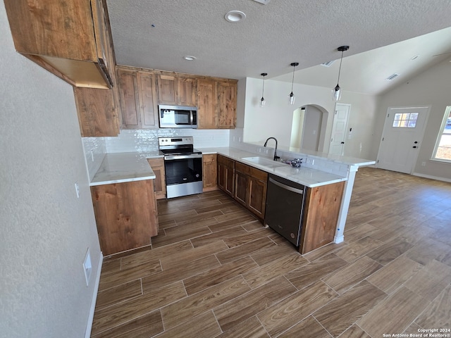 kitchen with appliances with stainless steel finishes, sink, kitchen peninsula, hanging light fixtures, and vaulted ceiling