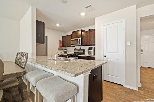 kitchen featuring light wood-type flooring, kitchen peninsula, appliances with stainless steel finishes, a kitchen breakfast bar, and sink