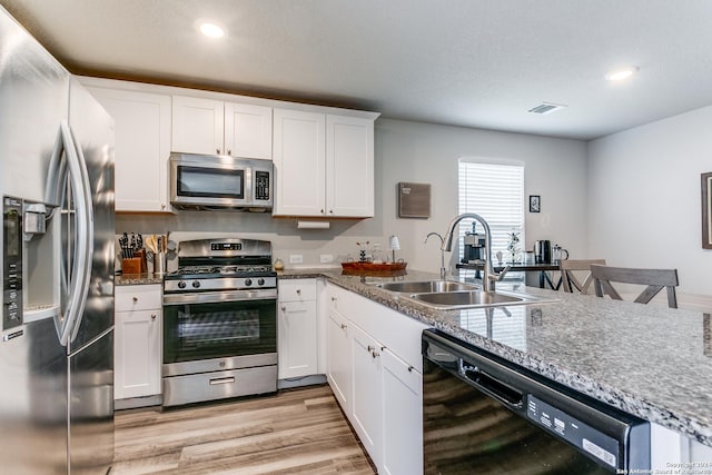 kitchen with sink, light wood-type flooring, appliances with stainless steel finishes, stone counters, and white cabinets