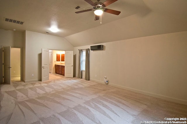 unfurnished bedroom featuring ceiling fan, ensuite bath, a wall unit AC, light carpet, and vaulted ceiling