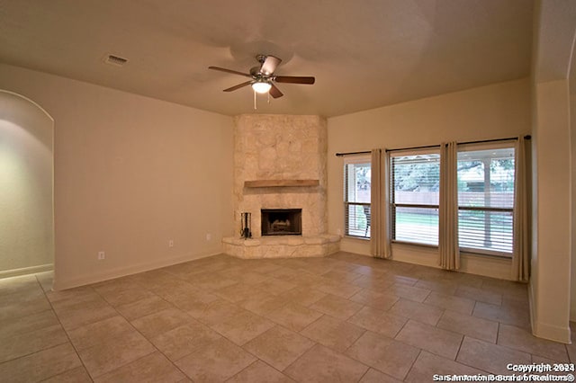 unfurnished living room with a stone fireplace, light tile patterned floors, and ceiling fan