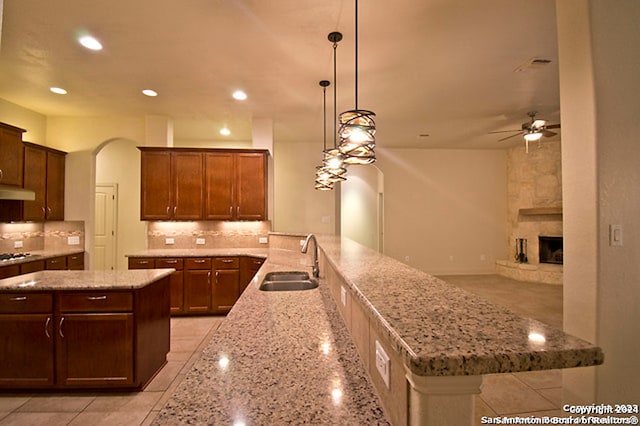 kitchen with a fireplace, ceiling fan, sink, kitchen peninsula, and backsplash