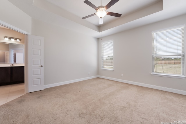 carpeted empty room with a wealth of natural light, ceiling fan, and a raised ceiling