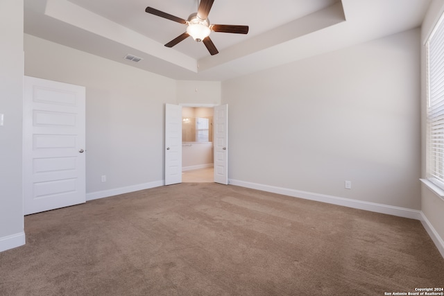 unfurnished bedroom featuring carpet flooring, connected bathroom, a raised ceiling, and ceiling fan