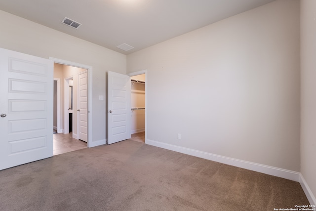 unfurnished bedroom with a spacious closet, a closet, and light colored carpet