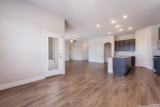 kitchen featuring dark brown cabinets, tasteful backsplash, ceiling fan, wood-type flooring, and a center island with sink