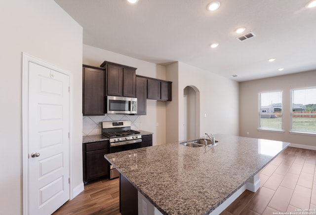 kitchen featuring decorative backsplash, sink, appliances with stainless steel finishes, and a center island with sink