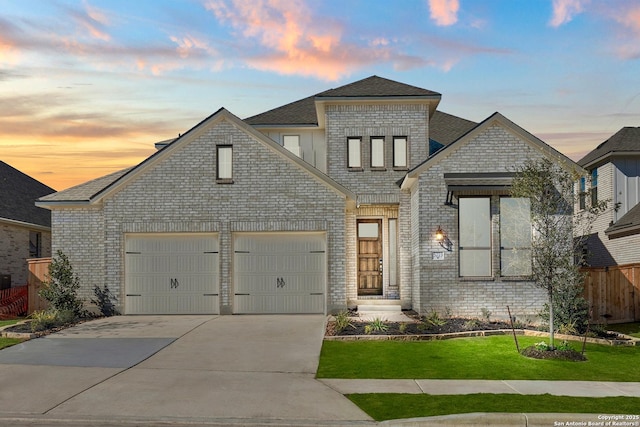 french provincial home with brick siding, concrete driveway, a lawn, an attached garage, and fence