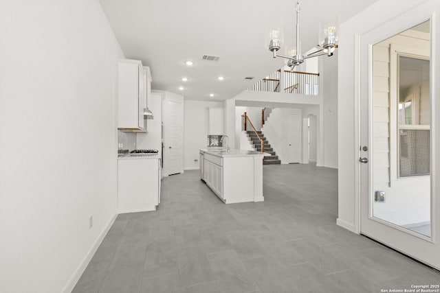 kitchen featuring sink, white cabinetry, a notable chandelier, an island with sink, and decorative light fixtures