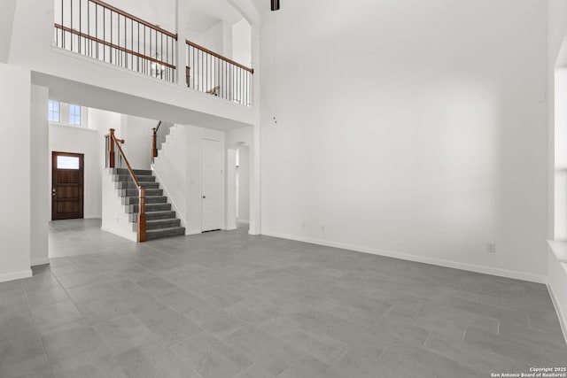 unfurnished living room featuring a high ceiling, stairs, and baseboards