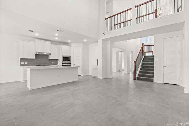 kitchen with arched walkways, visible vents, open floor plan, stainless steel microwave, and an island with sink