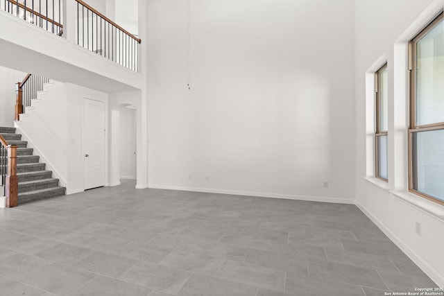 unfurnished living room featuring a towering ceiling, baseboards, and stairs