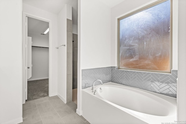 bathroom featuring tile patterned flooring, a spacious closet, baseboards, and a bath