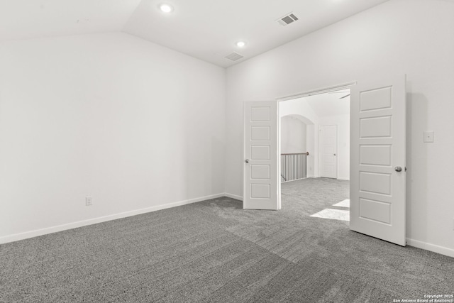 spare room with carpet floors, arched walkways, visible vents, vaulted ceiling, and baseboards