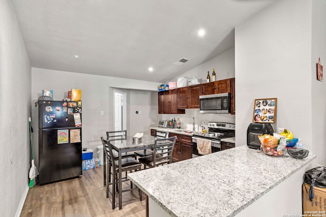 kitchen with lofted ceiling, light stone countertops, light wood-type flooring, and stainless steel appliances