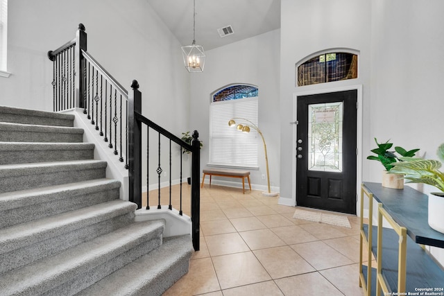 tiled foyer entrance featuring a chandelier and high vaulted ceiling