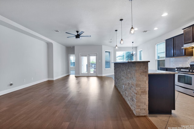 kitchen with tasteful backsplash, light wood-type flooring, an island with sink, stainless steel gas stove, and light stone countertops