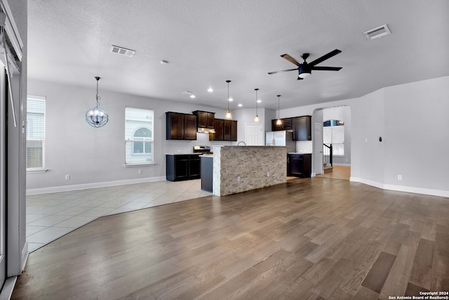 unfurnished living room featuring light wood-type flooring, ceiling fan with notable chandelier, and a textured ceiling