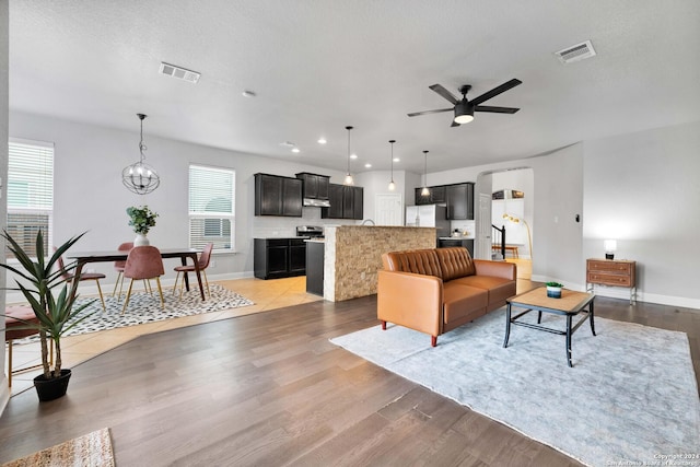 living room with ceiling fan with notable chandelier, a textured ceiling, and light wood-type flooring