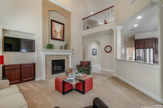 living room featuring a fireplace, light colored carpet, ornate columns, and a high ceiling