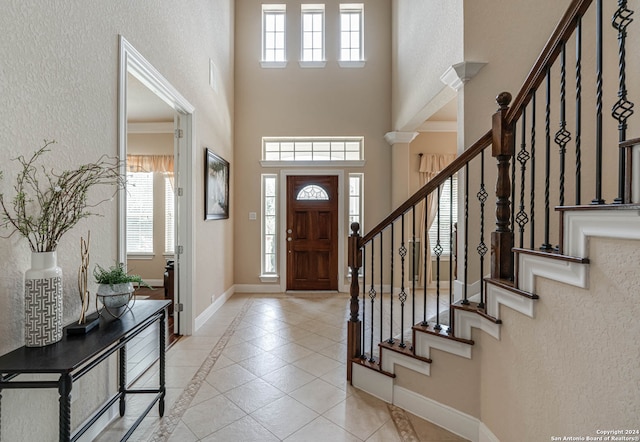 foyer with ornamental molding, light tile patterned floors, and a towering ceiling