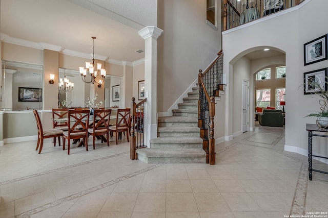 tiled entrance foyer featuring an inviting chandelier, decorative columns, crown molding, and a high ceiling