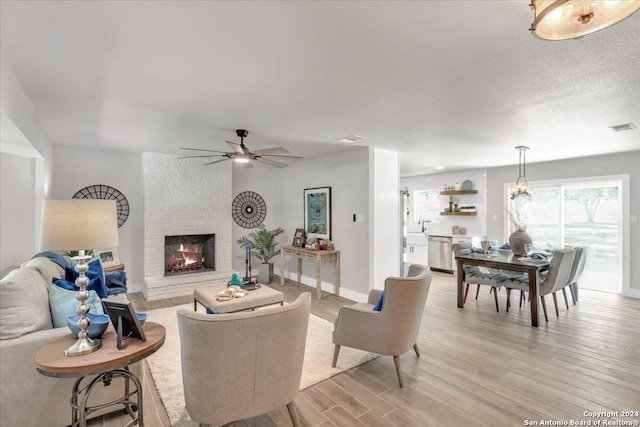 living room featuring light hardwood / wood-style flooring, a textured ceiling, ceiling fan, a brick fireplace, and brick wall