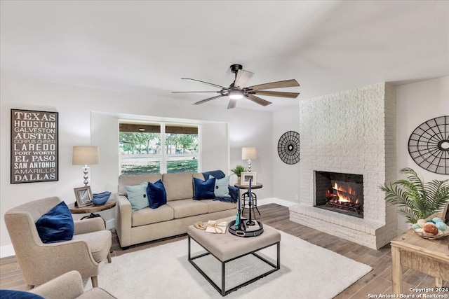 living room featuring wood-type flooring, a brick fireplace, brick wall, and ceiling fan