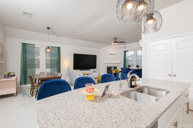 kitchen with sink, light tile patterned floors, light stone counters, and a kitchen island with sink