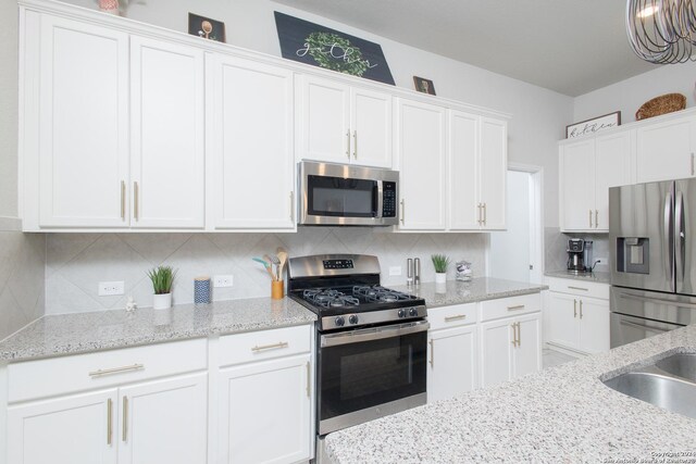 kitchen with white cabinets, decorative backsplash, light stone counters, and stainless steel appliances