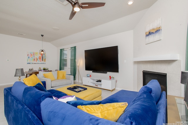 living room with a tiled fireplace, ceiling fan, and vaulted ceiling