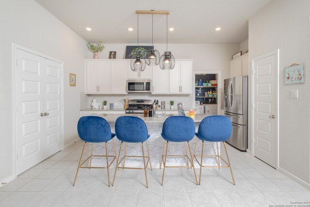 kitchen with decorative light fixtures, white cabinetry, stainless steel appliances, an island with sink, and light stone counters