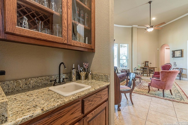 kitchen featuring sink, crown molding, light stone counters, light tile patterned floors, and ceiling fan