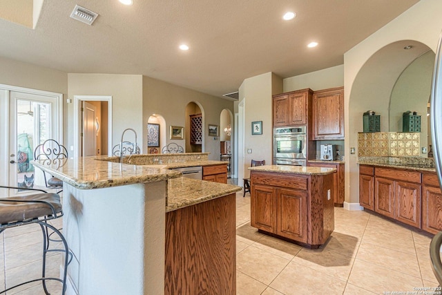 kitchen featuring a large island, light tile patterned floors, a breakfast bar area, stainless steel appliances, and light stone countertops