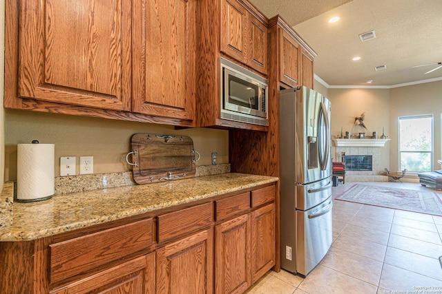 kitchen featuring light tile patterned flooring, light stone counters, crown molding, appliances with stainless steel finishes, and a tile fireplace