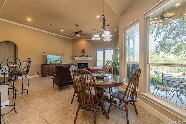 dining room with lofted ceiling, light tile patterned floors, crown molding, a fireplace, and ceiling fan with notable chandelier