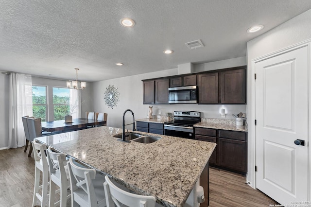 kitchen featuring sink, a kitchen island with sink, stainless steel appliances, dark brown cabinetry, and light wood-type flooring