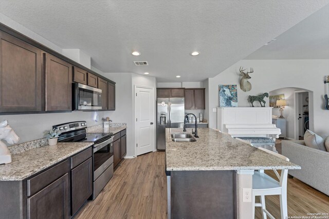 kitchen with dark brown cabinetry, sink, a center island with sink, light hardwood / wood-style flooring, and stainless steel appliances