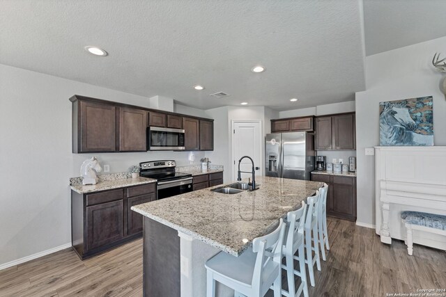 kitchen with a breakfast bar, an island with sink, sink, stainless steel appliances, and light stone countertops