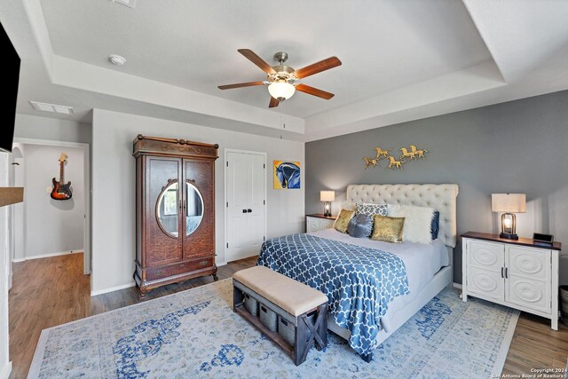 bedroom with dark wood-type flooring, ceiling fan, and a tray ceiling