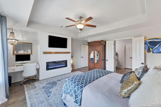 bedroom with a tray ceiling, wood-type flooring, built in desk, and ceiling fan