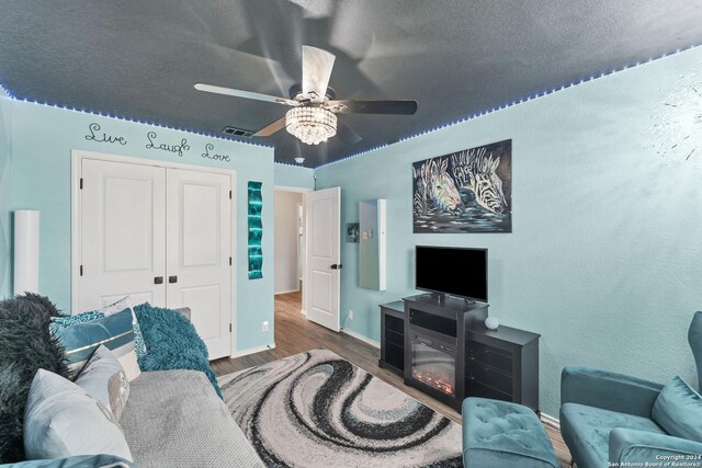 living room with dark wood-type flooring, ceiling fan, and a textured ceiling