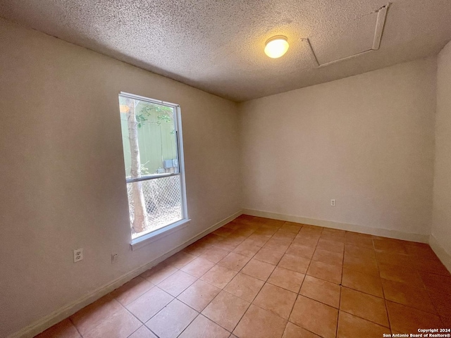 empty room featuring light tile patterned floors, a textured ceiling, plenty of natural light, and baseboards