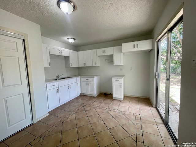 kitchen with white cabinets, sink, light tile patterned floors, and a textured ceiling